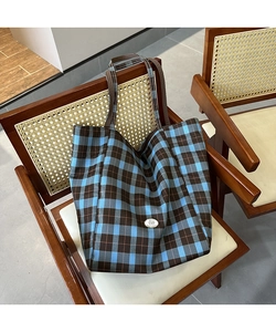 Détail d'un sac cabas en toile à carreaux bleu et marron suspendu à une chaise en rotin