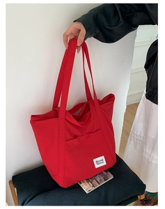 Detail of red nylon tote bag with white logo patch and dual shoulder straps