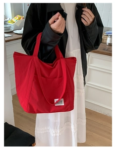 Red large capacity nylon tote bag with white woven label worn by a model in a bright kitchen