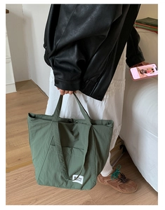 Close-up of olive green nylon tote bag featuring a brand label and large front pocket