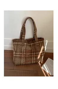 Detailed view of brown plaid wool tote bag with red embroidery in warm natural sunlight