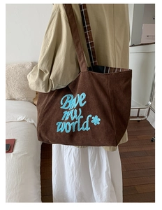 Detail of dark brown corduroy tote bag with light blue embroidery and plaid lining