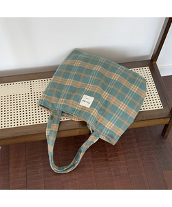 Detail of green and orange plaid tote bag showing woven label and wool-like texture