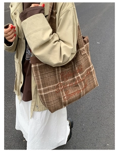 Close-up of brown plaid wool tote bag with floral embroidery on a textured fabric