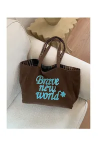 Detail of dark brown corduroy tote with blue embroidery on a minimalist sofa