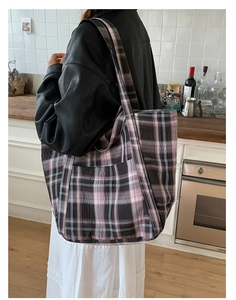 Detailed shot of a large plaid canvas tote bag worn by a model in a cozy kitchen setting