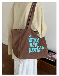Detail of brown corduroy tote bag with blue 'Brave new world' embroidery and wide strap