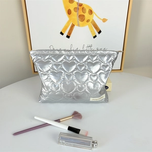 Detail of silver heart-quilted cosmetic bag with brand tag and zipper on a desk