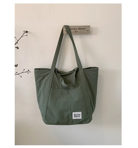 Close-up of minimalist green nylon tote bag with dual straps and woven brand label