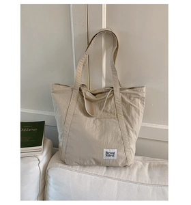 Detail view of beige nylon tote bag with Beyou Merci label on a white sofa scene