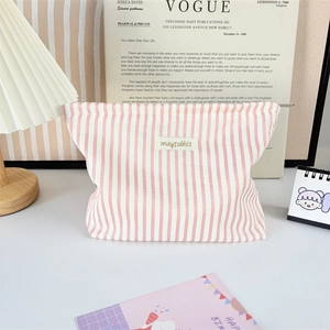 Pink striped fabric cosmetic bag with letter patch in a cozy home setting decor