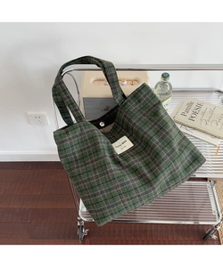 Detail of green plaid tote bag with textile texture and woven label on a metal rack