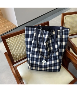 Détail du cabas en toile à carreaux bleus avec écusson logo sur une chaise en bois vintage