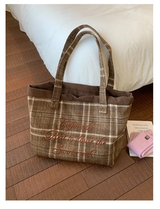 Macro shot of brown plaid tote bag featuring red embroidered text and corduroy trim details