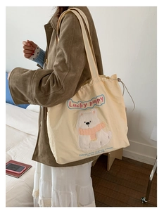 Detail of cream drawstring tote bag featuring an embroidered lucky puppy motif on canvas