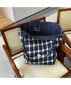 Détail du sac cabas en toile à carreaux avec logo brodé sur une chaise rustique