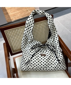 Close-up of polka dot canvas tote featuring a brown leather label and bow tie closure