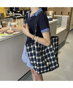 Détail d'un grand sac cabas en toile à carreaux bleu et beige porté à l'épaule dans un café