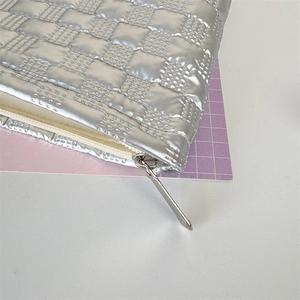 Detail of silver metallic quilted cosmetic bag with zipper and high-gloss leather texture