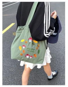 Detailed embroidery of mushrooms and acorns on a green nylon drawstring tote bag