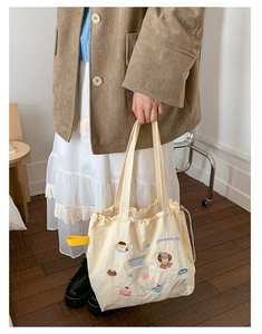 Detail of cute cartoon embroidery and yellow ribbon on cream drawstring tote bag