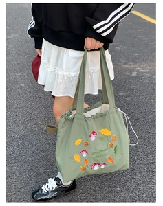 Close-up of olive green nylon tote featuring mushroom embroidery and drawstring detail