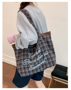 Detail of plaid tote bag featuring blue cursive embroidery on thick textured fabric