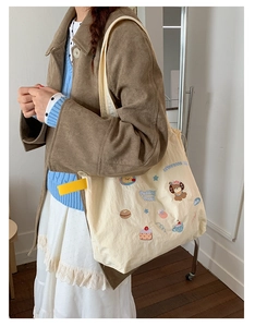 Detail of cute cartoon embroidery on a cream canvas tote bag with yellow accent strap
