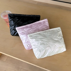 Quilted bow makeup bags in black, pink, and beige displayed on a wooden table