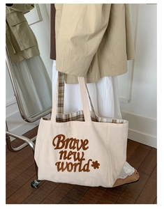 Detail of cream corduroy tote bag featuring brown embroidered text and plaid lining