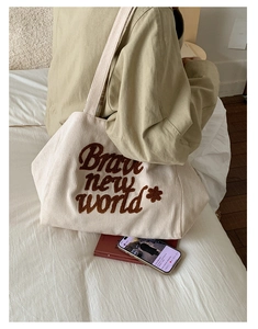 Detail of off-white corduroy tote bag featuring brown towel embroidery with slogan