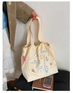 Detailed close-up of cute cat and cupcake embroidery on a beige drawstring tote bag