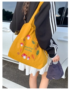 Detail of yellow nylon tote bag featuring autumn mushroom embroidery and sturdy shoulder strap