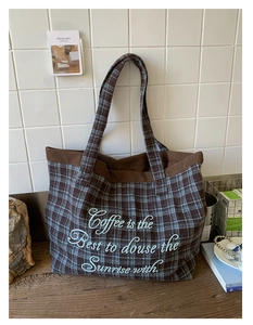 Detail of checkered tote bag featuring blue embroidery and brown corduroy trim finish