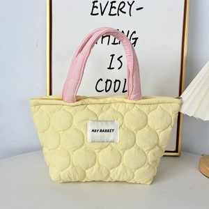 Quilted yellow handbag with pink handles featuring May Rabbit logo on a white desk