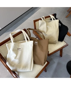Detailed display of canvas tote bags in off-white, brown, and black on a wooden chair