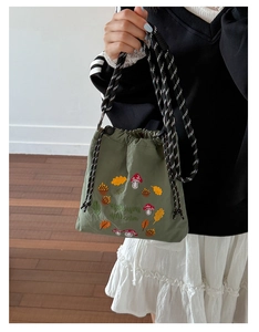 Detail of army green nylon bucket bag with mushroom embroidery and woven rope strap