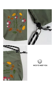 Detail of mushroom embroidery on olive green nylon bag with drawstring and metal ring