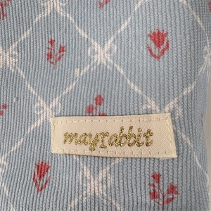 Detail of light blue corduroy fabric with bow pattern and mayrabbit brand woven label
