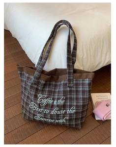 Detail of checkered tote bag with blue embroidery and corduroy trim on a bed