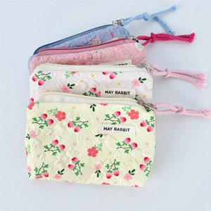 Detailed stack of floral and strawberry embossed canvas pouches with woven zipper pulls