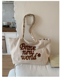 Detail of cream corduroy tote bag with Brave New World embroidery and plaid straps