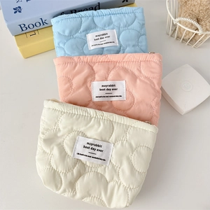 Close-up of three quilted cloud makeup bags in blue, pink, and beige with metal zippers