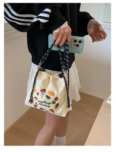 Detailed embroidery of mushrooms and leaves on a beige canvas drawstring bucket bag