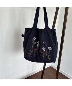 Close-up of floral embroidery on a black canvas tote bag with daisy and lily patterns