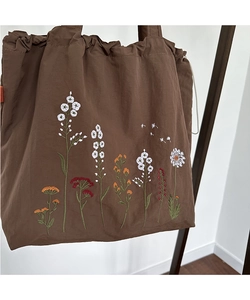 Detailed embroidery of colorful wild flowers on a dark brown nylon drawstring tote bag
