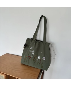 Detail of floral embroidery on a dark green canvas tote bag with drawstring closure