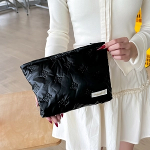 Close-up of black quilted handheld cosmetic bag with bow patterns and zipper detail