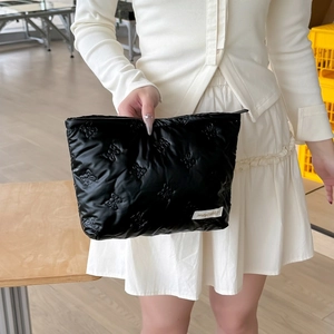 Close-up of black quilted makeup bag with bow patterns and brand tag held by hand