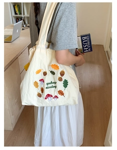Detailed close-up of mushroom and oak leaf embroidery on the beige nylon tote bag